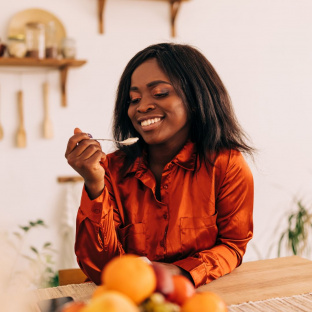 Picture of a black woman enjoying a meal at home, representing cooking at home to make your salary last longer.