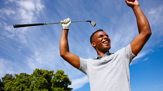 A golfer smiling as he reaches the 18th hole, capturing the sense of accomplishment in "playing the long game in investing" and achieving one's financial goals after years of disciplined effort.