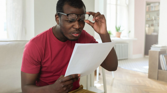 A person examining documents suspiciously, demonstrating how to spot the "5 signs of a scam" in suspicious offers.